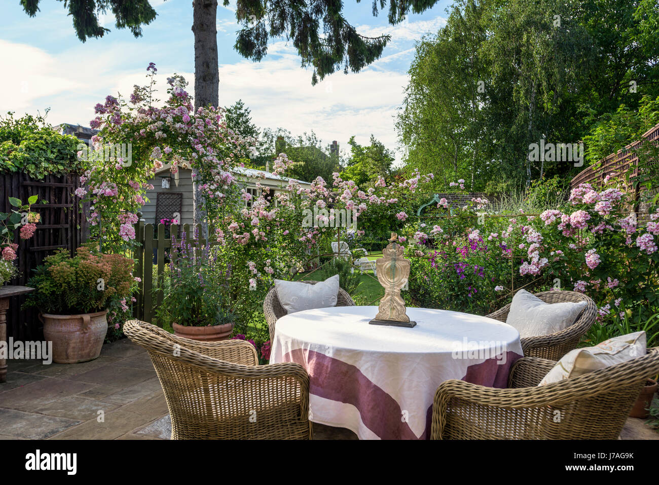 Poltrone in vimini intorno al tavolo in inglese il giardino murato con arco di rose Foto Stock