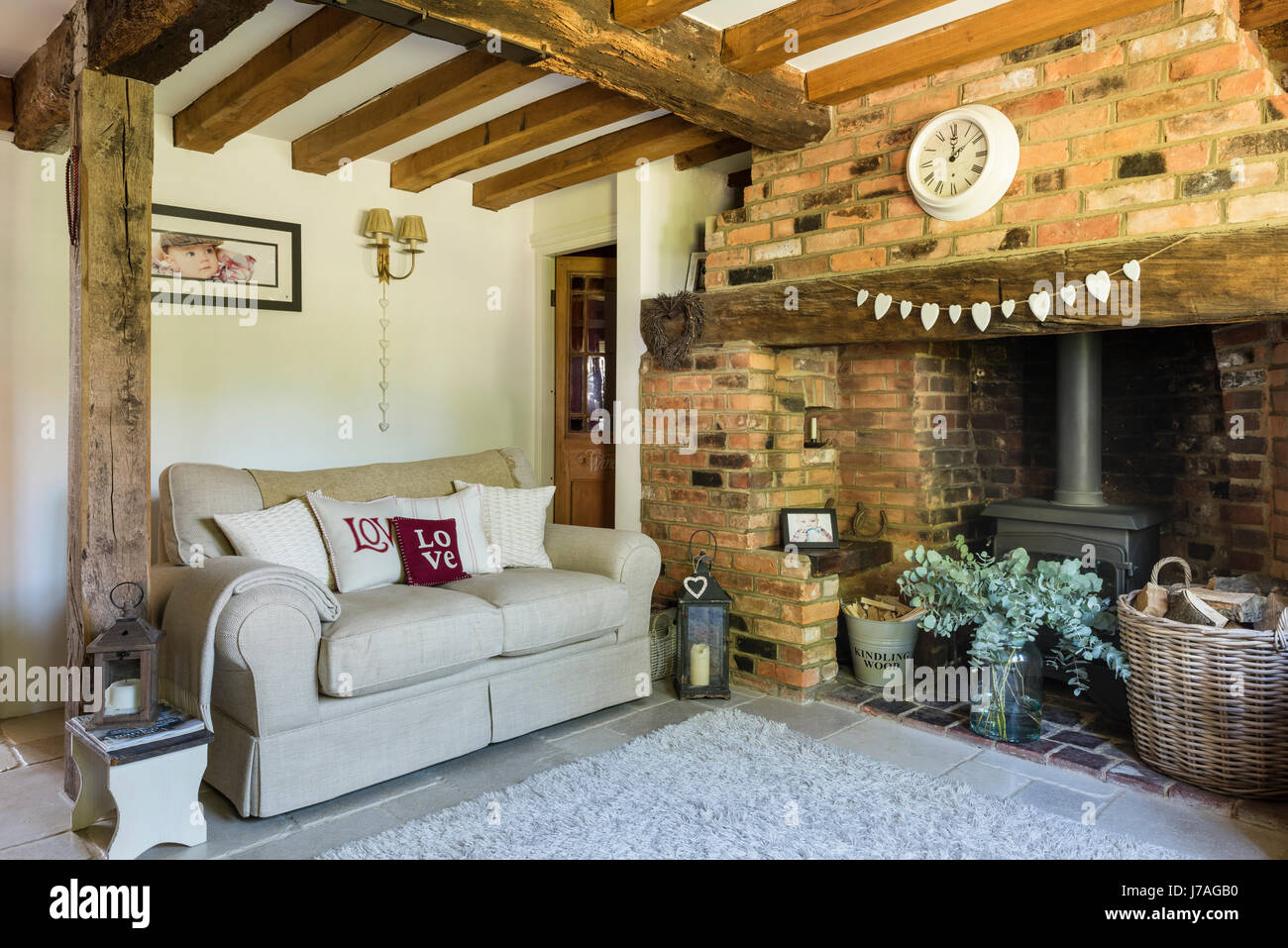 Accogliente salotto con caminetto inglenook, esposto un muro di mattoni e travi di legno sul soffitto. La crema il divano è da Laura Ashley e il tappeto da John Lewi Foto Stock