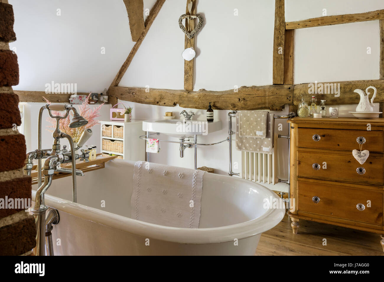 Bagno con soffitto a volta con le antiche travi esposte, muro di mattoni e roll-top bagno francese. Foto Stock