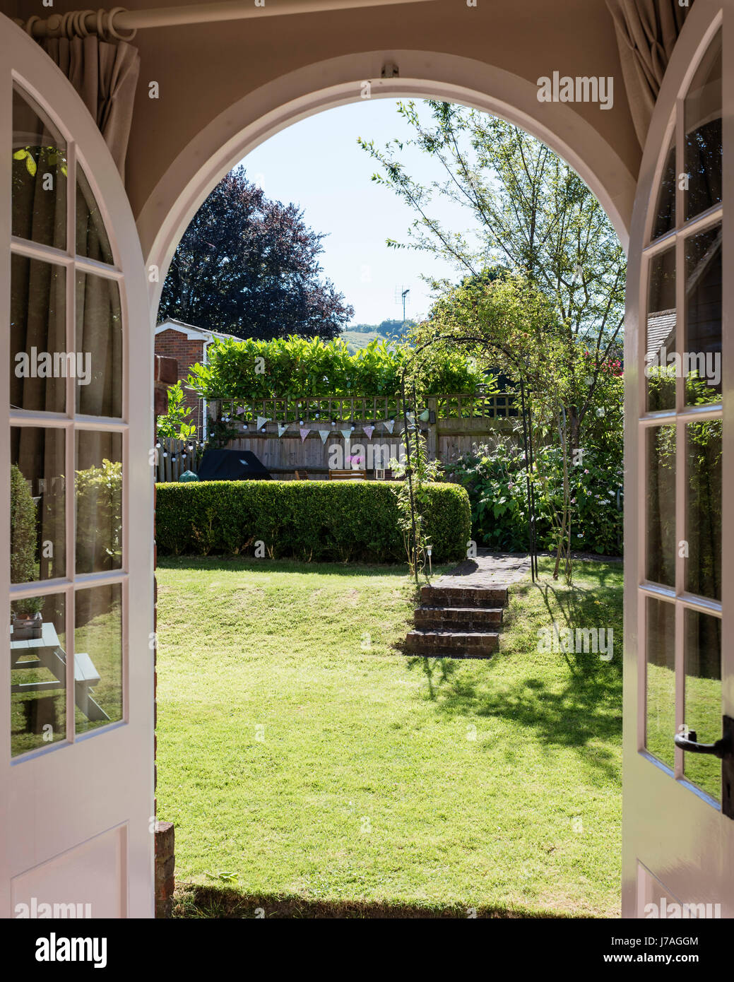 Vista attraverso arcuata di porte francesi per paese piccolo giardino Foto Stock