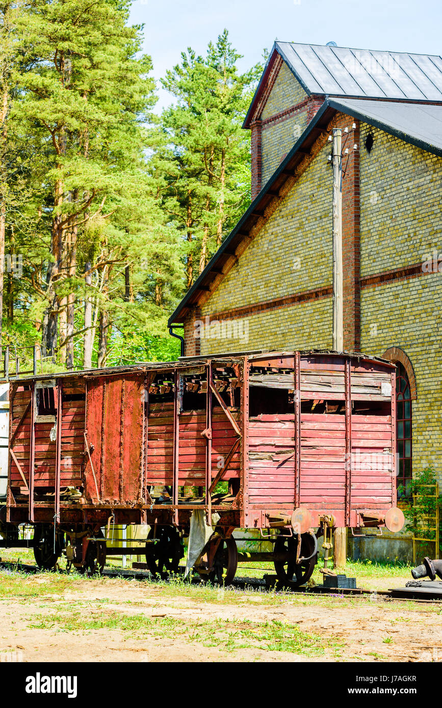 Abbandonato red vintage boxcar di legno in piedi sul binario ferroviario all'esterno in mattoni gialli con la foresta in background. Foto Stock