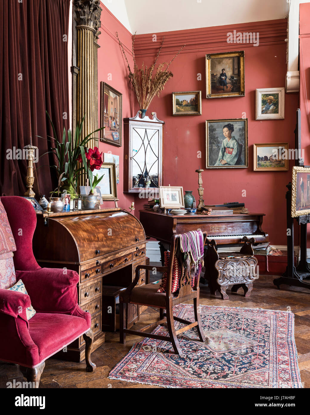 Velluto rosso poltrona nel disegno della Boemia toom con baby grand piano, secretaire e tappeto persiano. Le pareti sono dipinte in Farrow & Ball Libro di R Foto Stock