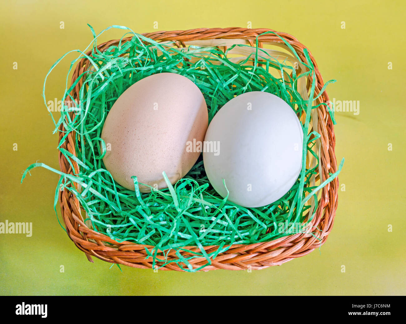 Luce verde Duck egg e marrone chiaro uovo di pollo, marrone cesto con erba, sfondo giallo. Foto Stock