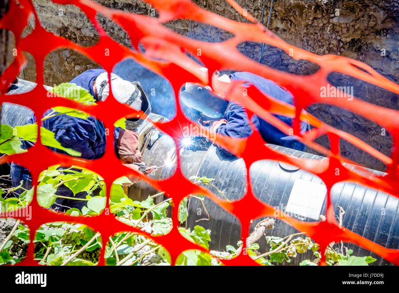 I saldatori sono in trincea che operazioni di saldatura ad arco pipeline. Spazio ristretto con Orange, plastica, rete di sicurezza Foto Stock