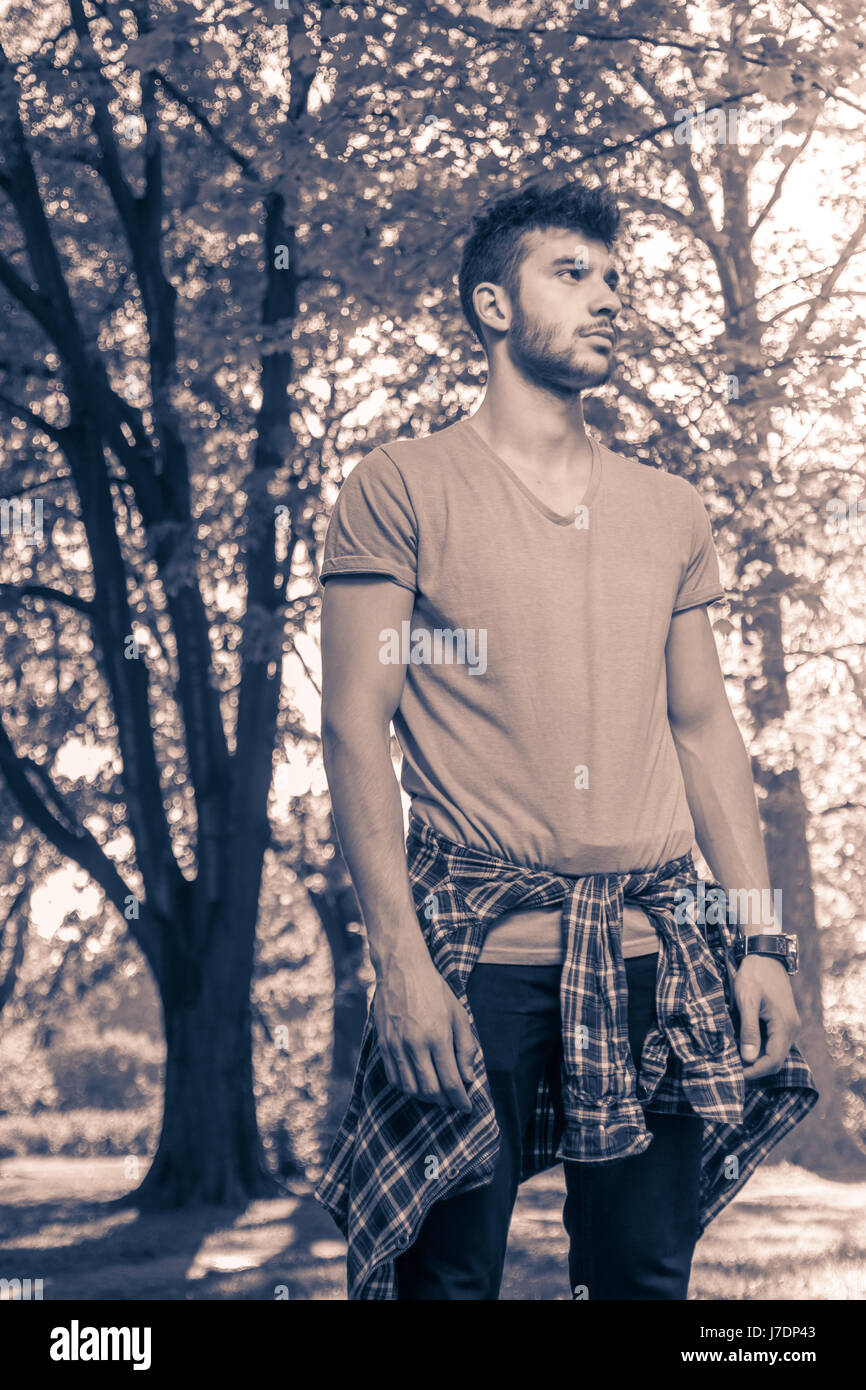 Un giovane adulto solo l'uomo abiti casual, guardando dal lato, parco natura, immagine in bianco e nero Foto Stock