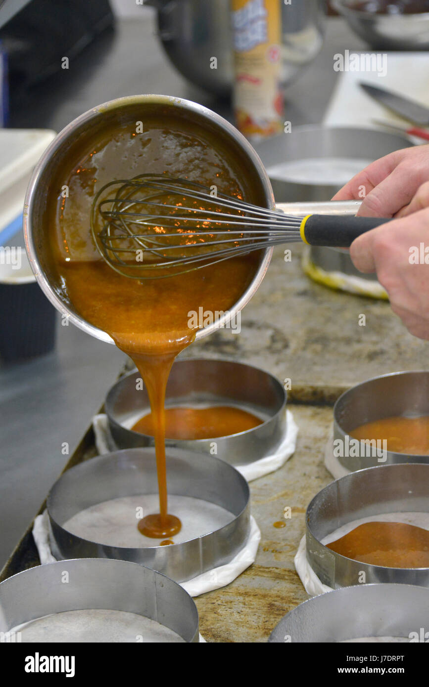 Una vista verticale di un fornaio mani con una frusta, versando la miscela di torta circolare in teglie. Foto Stock