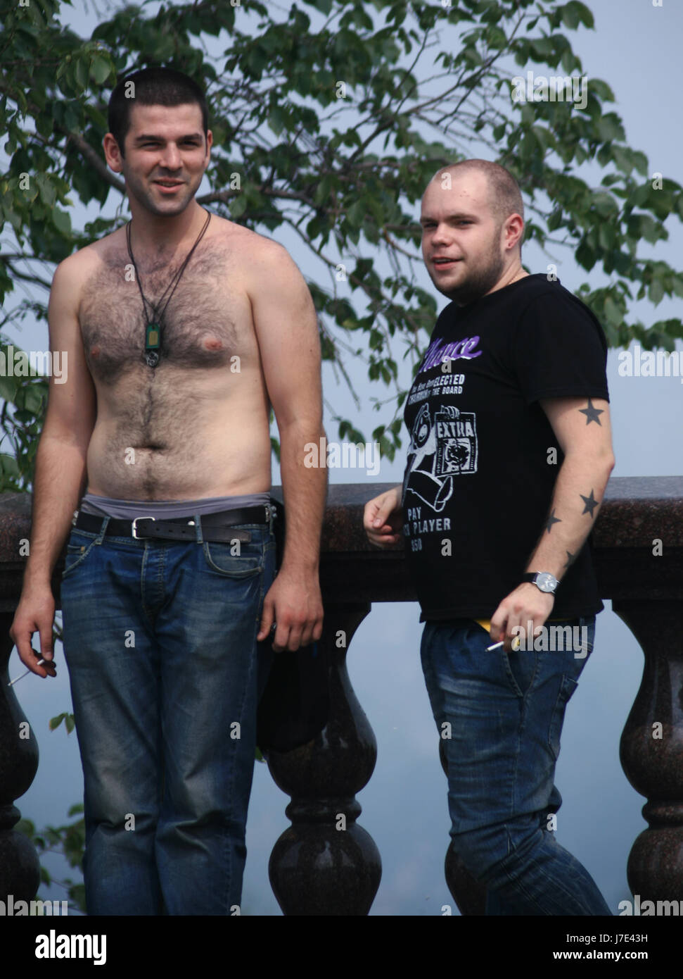 Due brutali giovani uomini, gli appassionati di musica rock sono un riposo nel parco della città nel caldo del giorno. Entrambi di buon umore anche sorridere al fotografo. Foto Stock