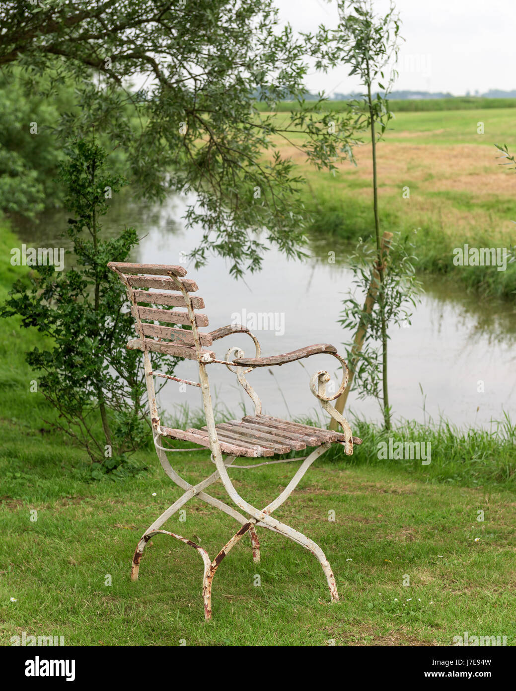 Vecchia sedia con peeling vernice su riverbank nel paesaggio rurale Foto Stock