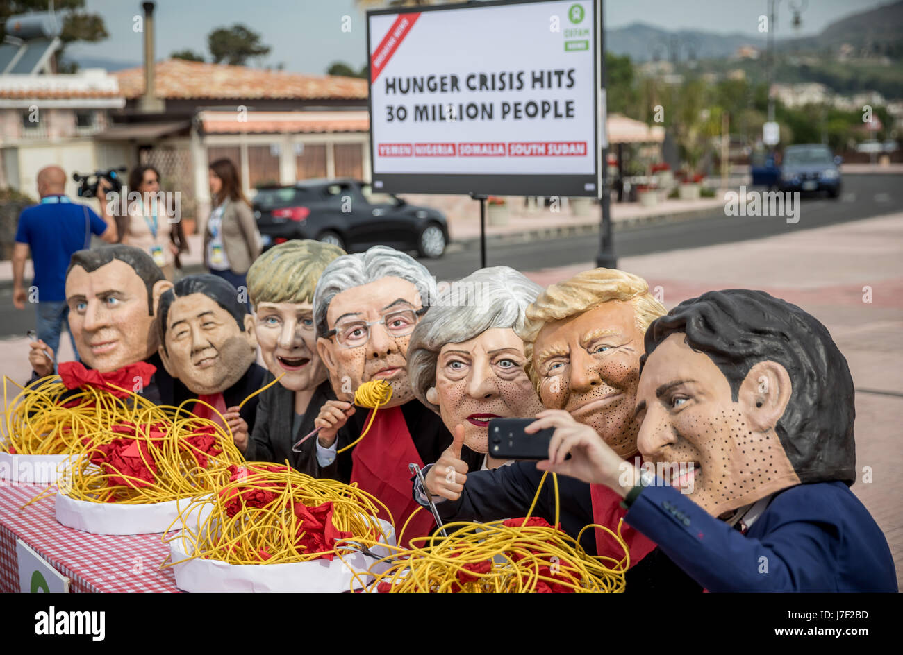 Taormina, Italia. 25 Maggio, 2017. Gli attivisti di Oxfam indossare maschere del G7-capi del presidente francese Emmanuel Macron (L-R), Giappone il Primo Ministro Shinzo Abe, Tedesco il Cancelliere Angela Merkel, Italia Il Ministro Presidente Paoplo Gentilono, Gran Bretagna il Primo Ministro Teresa maggio, US-presidente Donald Trump e Canada il Primo Ministro Justin Trudeau sedersi su un set di simbolicamente la tabella nella parte anteriore di piastre di spaghetti a Taormina, Italia, 25 maggio 2017. Credito: dpa picture alliance/Alamy Live News Foto Stock