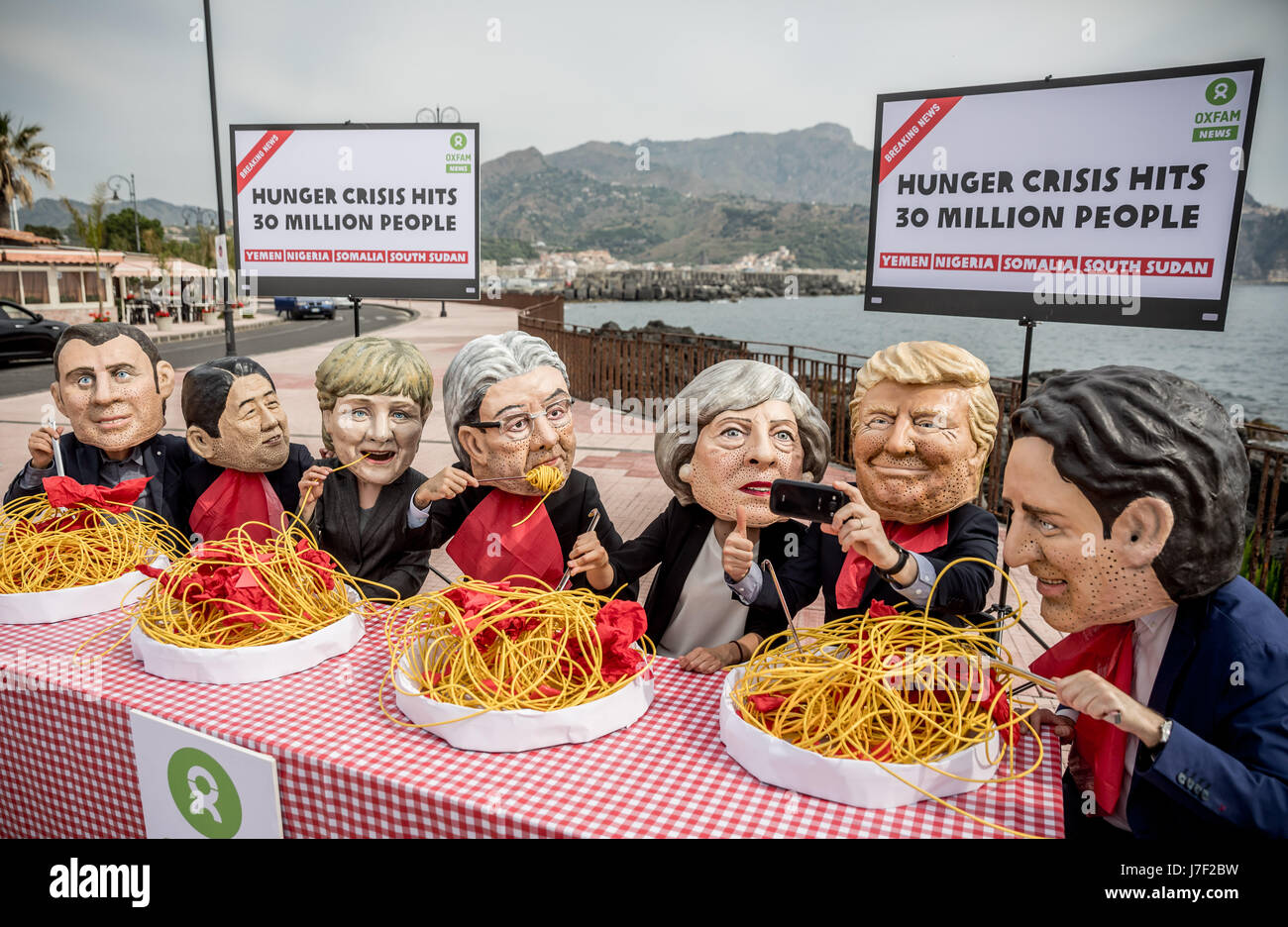 Taormina, Italia. 25 Maggio, 2017. Gli attivisti di Oxfam indossare maschere del G7-capi del presidente francese Emmanuel Macron (L-R), Giappone il Primo Ministro Shinzo Abe, Tedesco il Cancelliere Angela Merkel, Italia Il Ministro Presidente Paoplo Gentilono, Gran Bretagna il Primo Ministro Teresa maggio, US-presidente Donald Trump e Canada il Primo Ministro Justin Trudeau sedersi su un set di simbolicamente la tabella nella parte anteriore di piastre di spaghetti a Taormina, Italia, 25 maggio 2017. Credito: dpa picture alliance/Alamy Live News Foto Stock