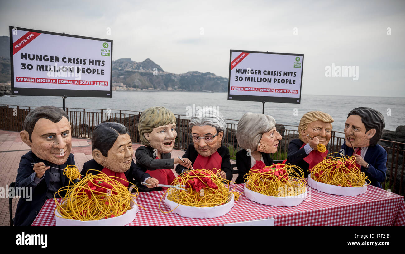 Taormina, Italia. 25 Maggio, 2017. Gli attivisti di Oxfam indossare maschere del G7-capi del presidente francese Emmanuel Macron (L-R), Giappone il Primo Ministro Shinzo Abe, Tedesco il Cancelliere Angela Merkel, Italia Il Ministro Presidente Paoplo Gentilono, Gran Bretagna il Primo Ministro Teresa maggio, US-presidente Donald Trump e Canada il Primo Ministro Justin Trudeau sedersi su un set di simbolicamente la tabella nella parte anteriore di piastre di spaghetti a Taormina, Italia, 25 maggio 2017. Con questa azione gli attivisti si desidera sollevare la consapevolezza per la carestia in Africa. Credito: dpa picture alliance/Alamy Live News Foto Stock