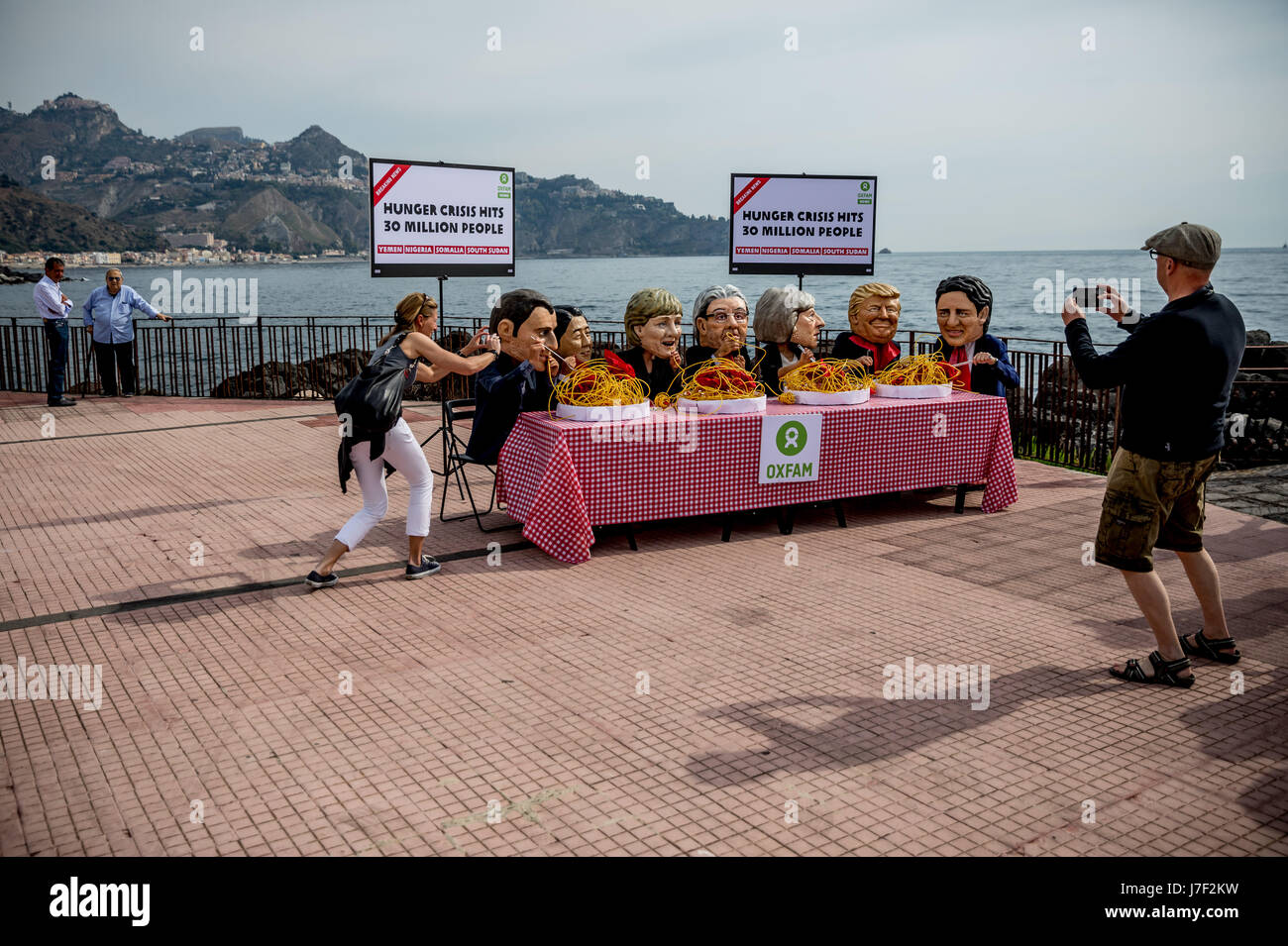 Taormina, Italia. 25 Maggio, 2017. Gli attivisti di Oxfam indossare maschere del G7-capi del presidente francese Emmanuel Macron (L-R), Giappone il Primo Ministro Shinzo Abe, Tedesco il Cancelliere Angela Merkel, Italia Il Ministro Presidente Paoplo Gentilono, Gran Bretagna il Primo Ministro Teresa maggio, US-presidente Donald Trump e Canada il Primo Ministro Justin Trudeau sedersi su un set di simbolicamente la tabella nella parte anteriore di piastre di spaghetti a Taormina, Italia, 25 maggio 2017. Credito: dpa picture alliance/Alamy Live News Foto Stock