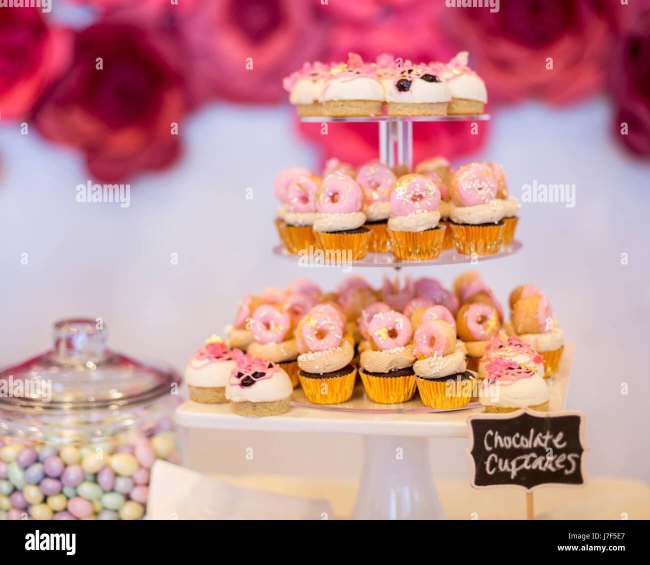 Mini tortini di cioccolato e rabboccato con mini ciambelle rosa su una tavola da dessert. Essi vengono visualizzate su un display a più livelli vassoio. Vi è un bel segno della lavagna. Foto Stock