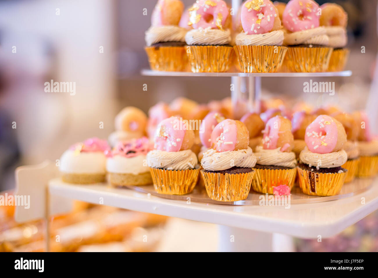 Mini tortini di cioccolato e rabboccato con mini ciambelle rosa su una tavola da dessert. Essi vengono visualizzate su un display a più livelli vassoio. Foto Stock