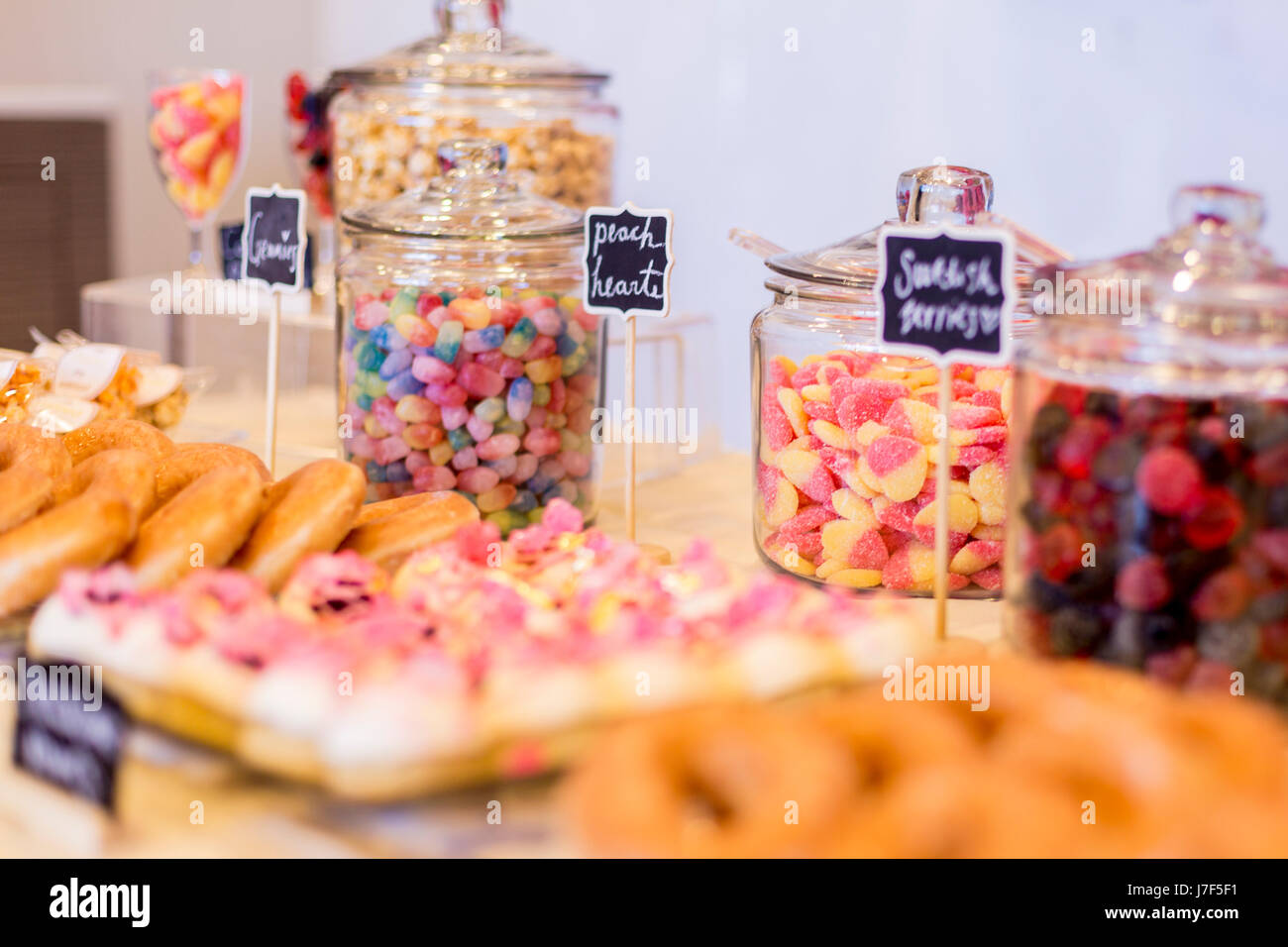 Caramelle colorate in vasi su un tavolo da dessert con ciambelle, cookie e popcorn. Ci sono simpatici chalkboard segni. Foto Stock