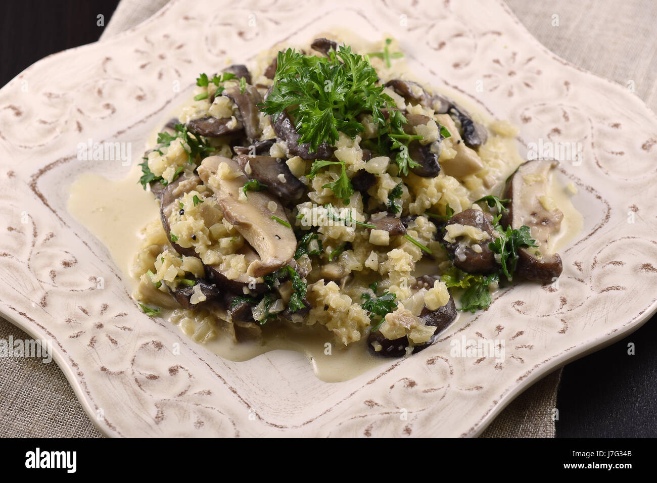 Il cavolfiore risotto con 3 tipi di funghi e prezzemolo su un piatto bianco Foto Stock