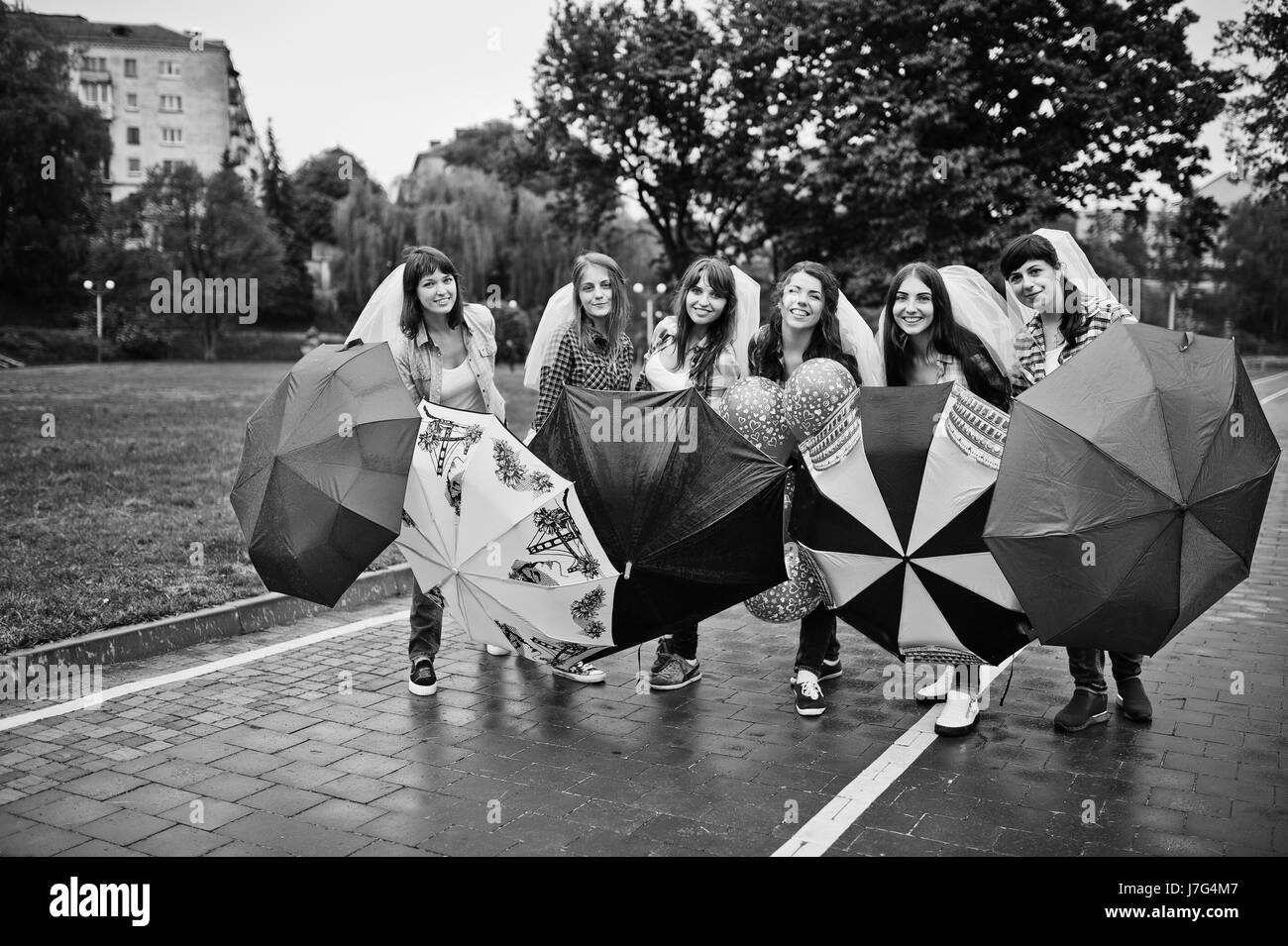 Un gruppo di sei ragazze divertendosi al partito di gallina, con ombrello sotto la pioggia e palloncini. Foto Stock