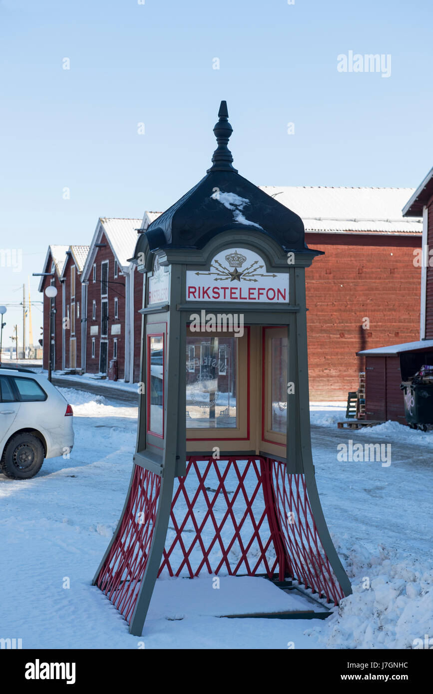 Storica cabina telefonica svedese "Rikstelefon" a Hudiksvall durante l'inverno, circondata dalla neve e dai tradizionali edifici in legno rosso Foto Stock