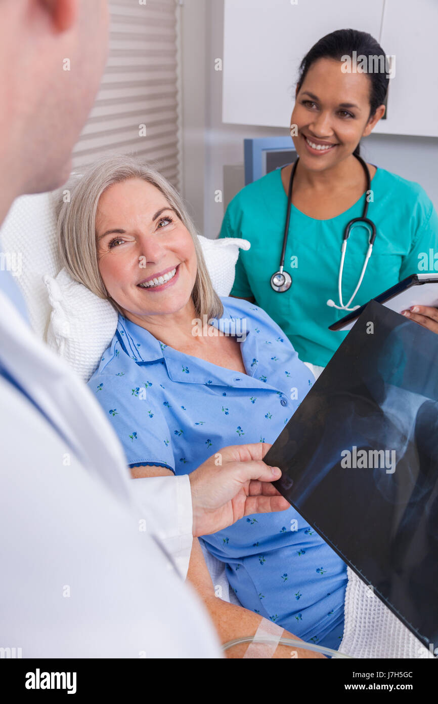 Felice donna senior il recupero del paziente nel letto di ospedale con connettore maschio di tipo medico e infermiere femmina guardando anca x-ray Foto Stock