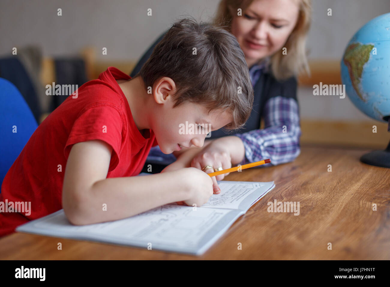 Madre figlio aiuta a imparare a casa dal foglio di lavoro Foto Stock