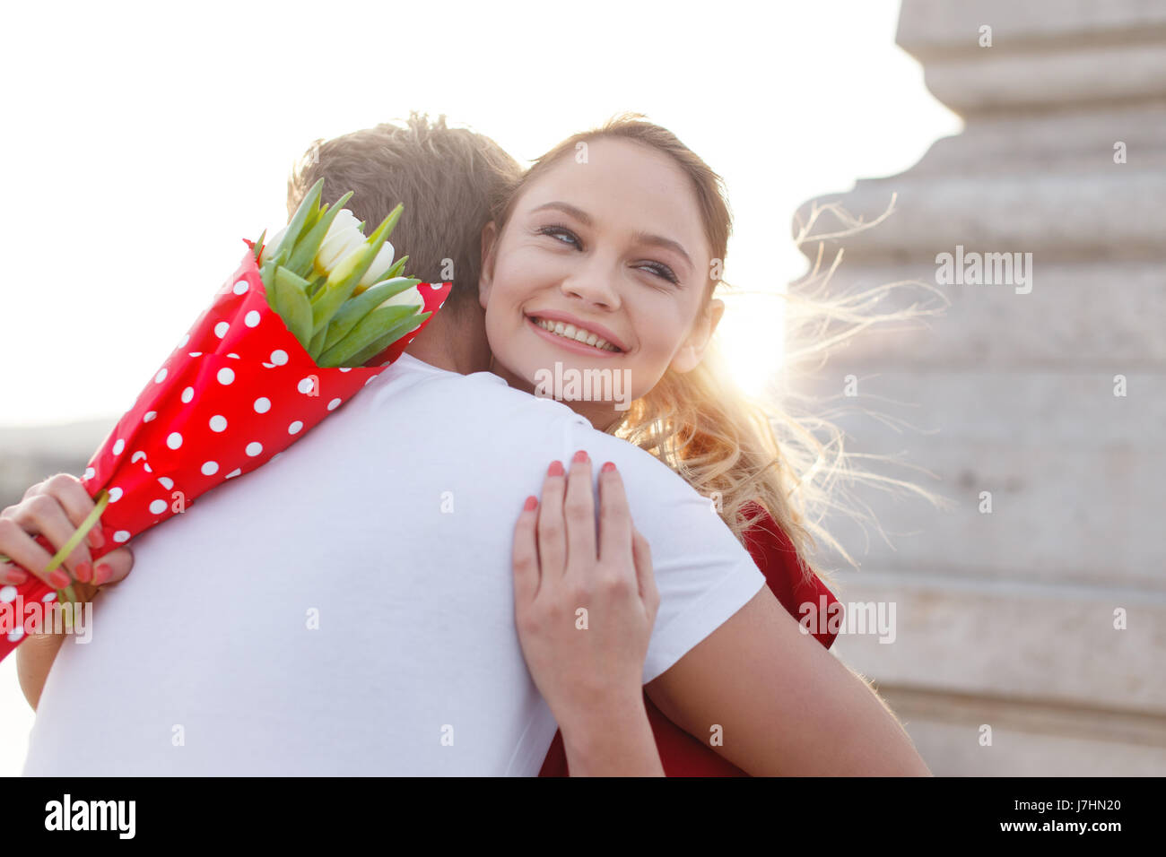 Donna felice con bouquet abbracciato da ragazzo per esterno Foto Stock