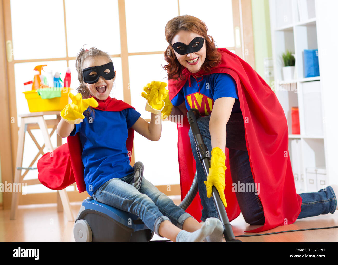 Kid ragazza e sua madre usurata costumi di supereroi. Carino bambino helper e donna rendono la pulizia camera e hanno un divertimento. Foto Stock