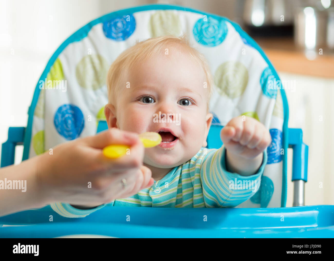 La famiglia e il concetto di nutrizione - madre alimentazione Cucchiaio piccolo bambino seduto nel seggiolone a casa Foto Stock
