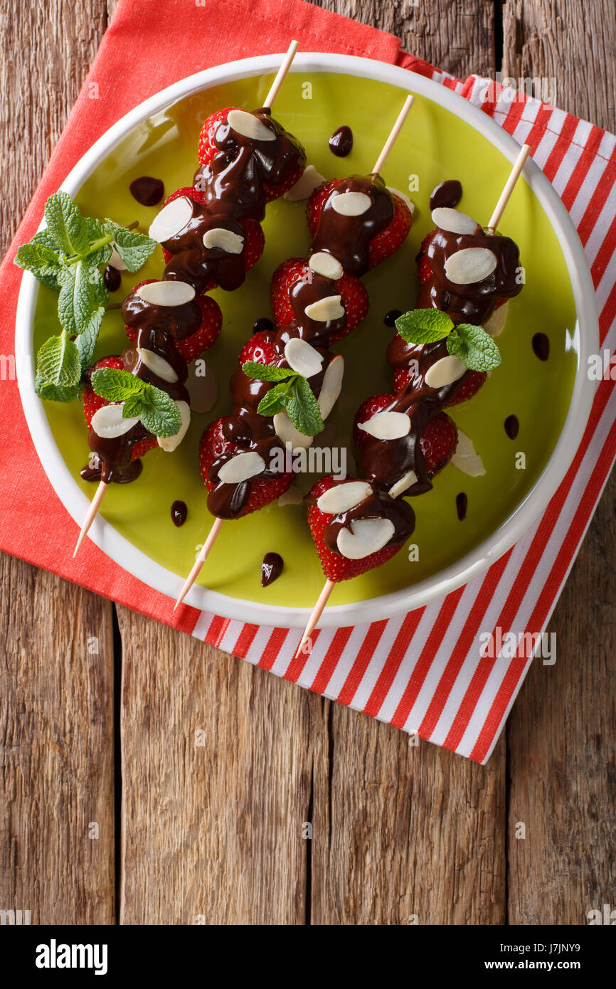 Spiedini con fragole fresche sono decorate con cioccolato, menta e mandorle su una piastra. Vista verticale da sopra Foto Stock