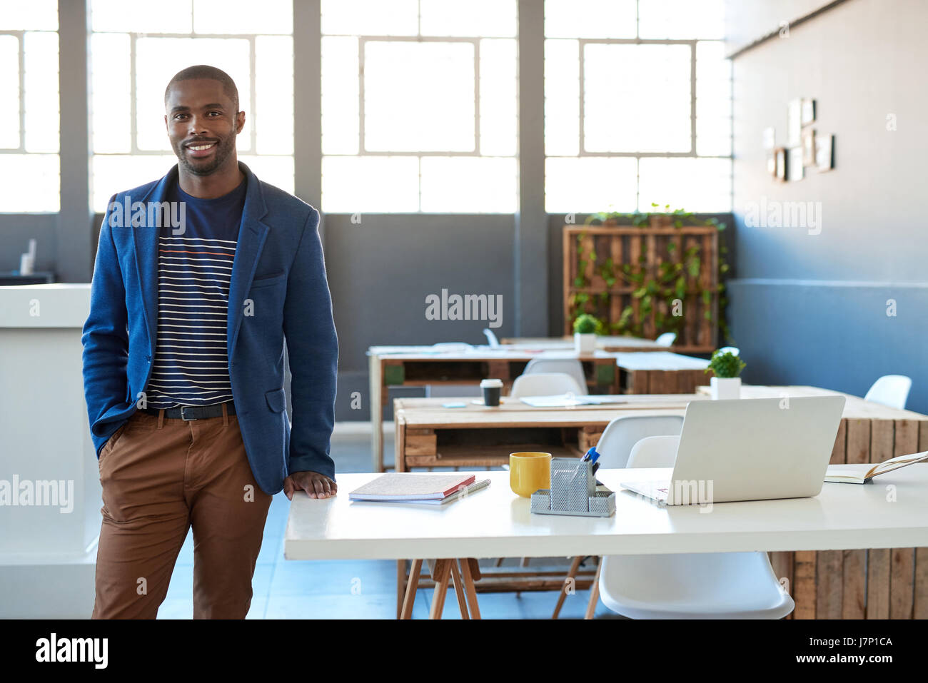 Fiducioso giovane imprenditore africani in piedi e sorridente in ufficio Foto Stock