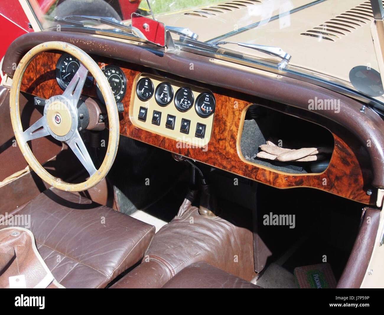 Questa immagine mostra il cruscotto di una Morgan 1977 4/4, una classica auto sportiva britannica. Il Morgan 4/4 è noto per il suo design senza tempo, i pannelli in legno e la configurazione aperta a due posti. Il numero di targa GF 04 LY identifica questo veicolo specifico. Foto Stock