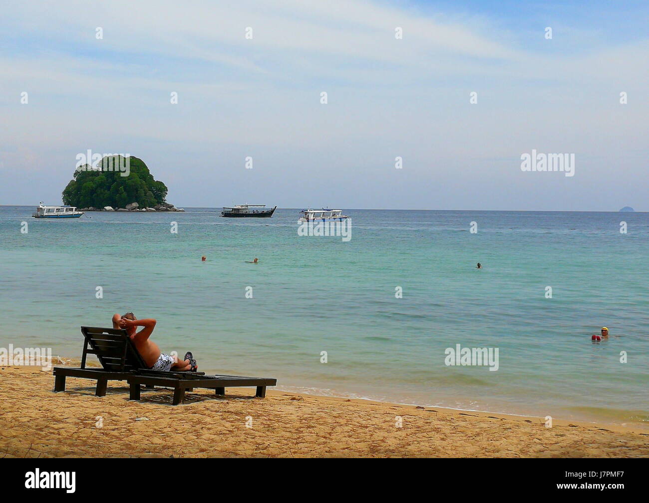 Un singolo turista di relax presso la spiaggia di Isola di Tioman, Malaysia, su una sedia a sdraio, mentre un altro di fare una nuotata nel bel mare blu. Foto Stock