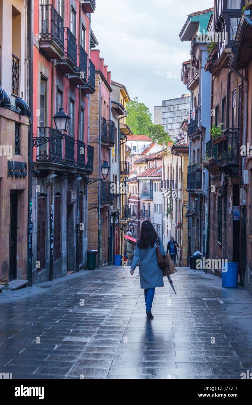 Una giovane donna con ombrello a piedi dalla fotocamera, Calle San José in città medievale, Oviedo, Asturias, Spagna Foto Stock