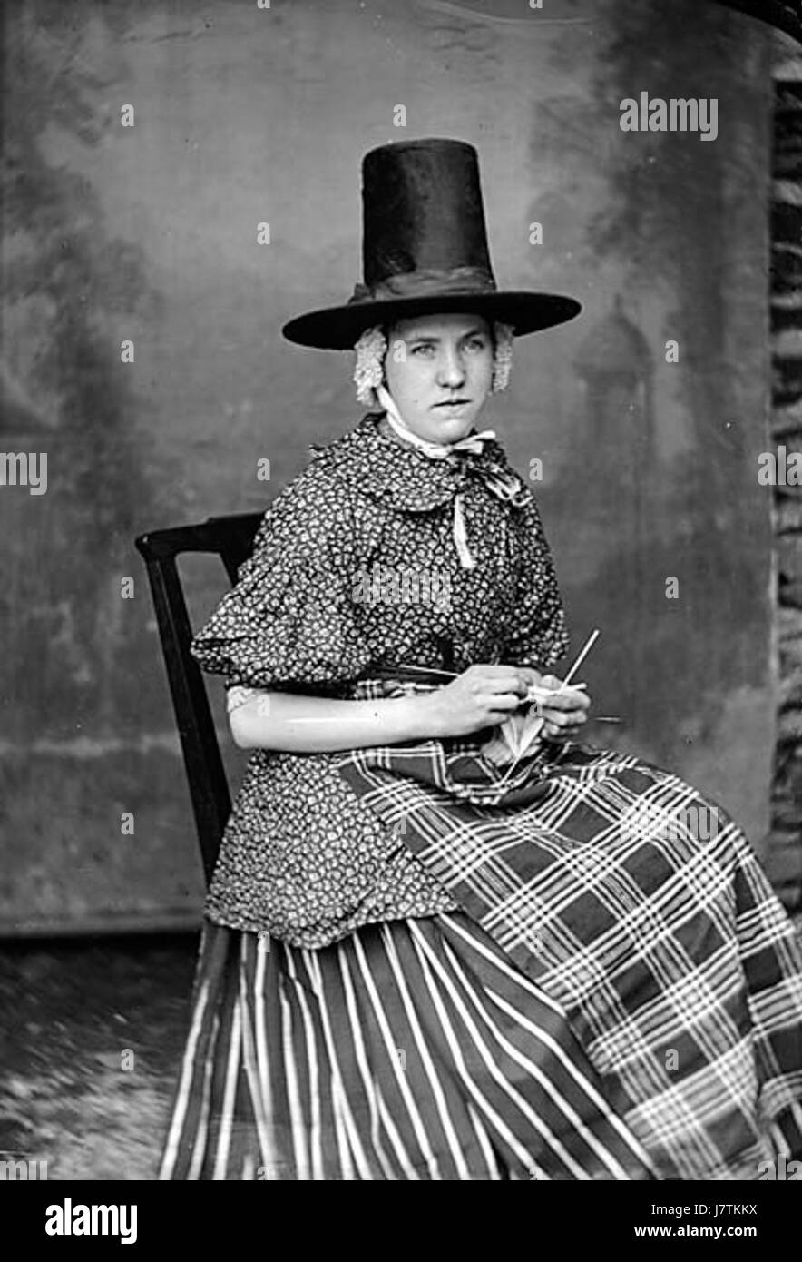 Questa immagine raffigura una donna in tradizionale abito nazionale, raffigurata dall'artista S A Jones. È impegnata nell'atto di lavorare a maglia, un mestiere che ha un significato culturale in molte società. Foto Stock