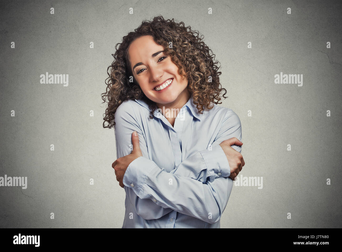 Closeup ritratto fiducioso donna sorridente holding abbracciando sé isolato muro grigio Sfondo. Positivo emozione umana, l'espressione del viso, sensazione, re Foto Stock