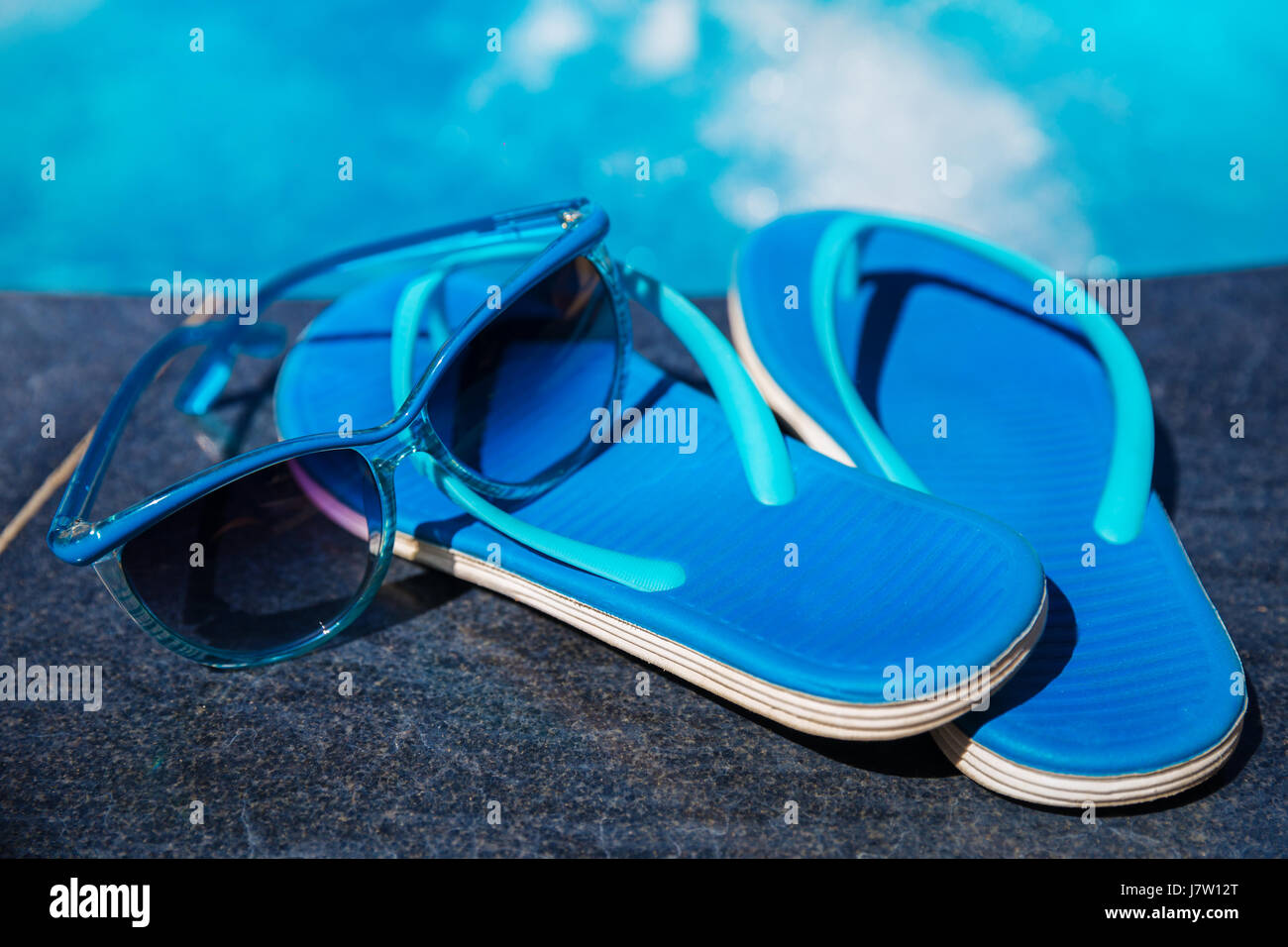 Pantofole blu e occhiali da sole vicino alla piscina - vacanza concept Foto Stock