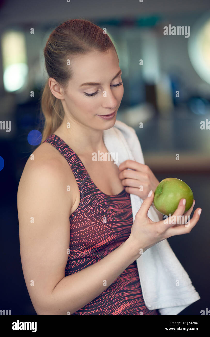 Montare sportivo da donna giovane contemplando una fresca mela verde lei tiene in mano dopo aver lavorato in palestra in un concetto di dieta sana e acti Foto Stock