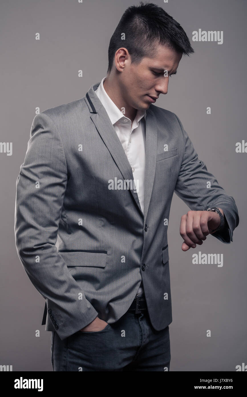 Un giovane uomo adulto, abiti formali, cappotto, una camicia bianca, la parte superiore del corpo e sfondo grigio, studio, guardando a guardare Foto Stock