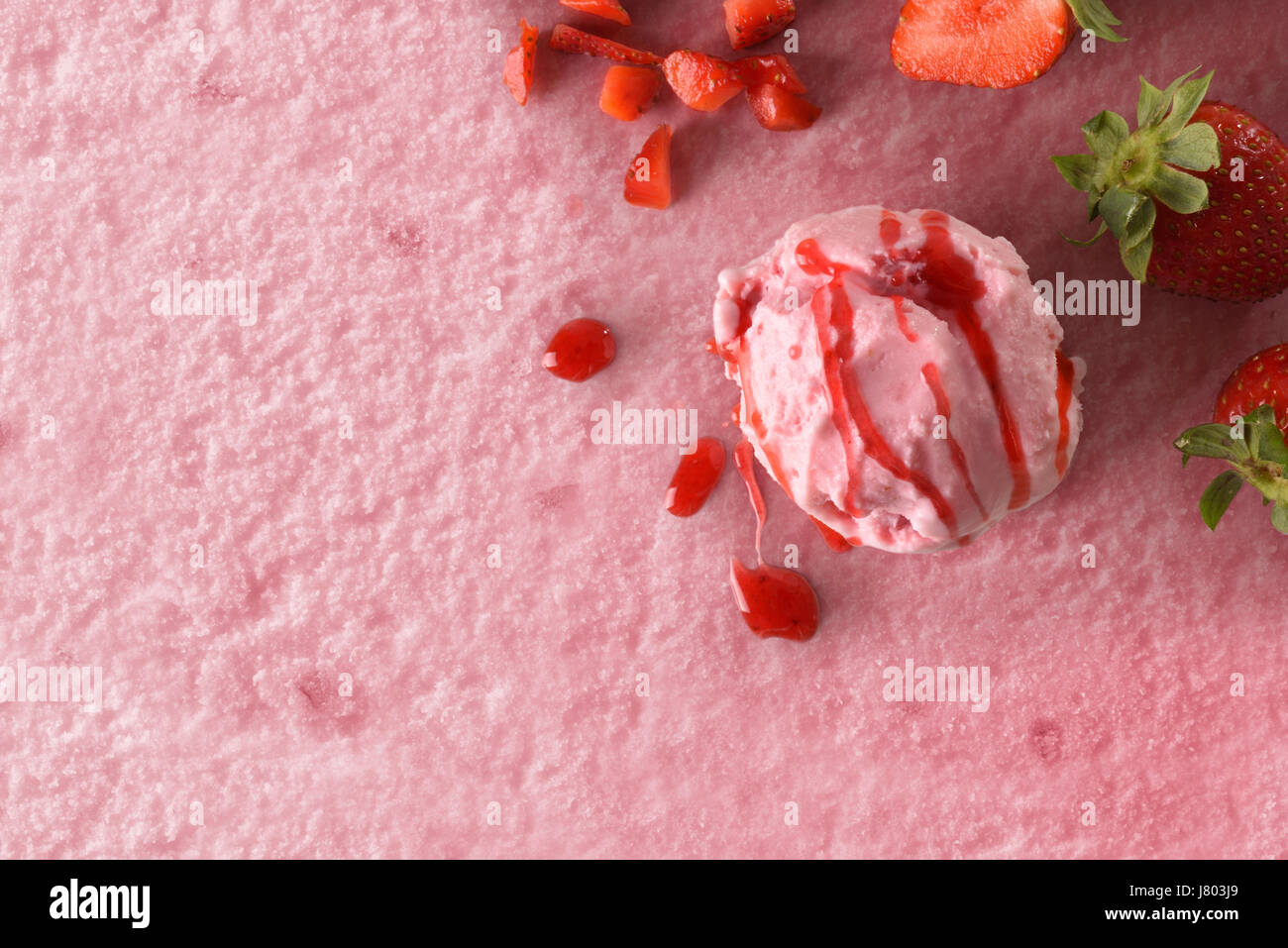 Gelato alla fragola aromatizzato sfondo texture con sfera. Guarnito con pezzi di frutta fragola e sciroppo. Vista dall'alto. Composizione orizzontale. Foto Stock