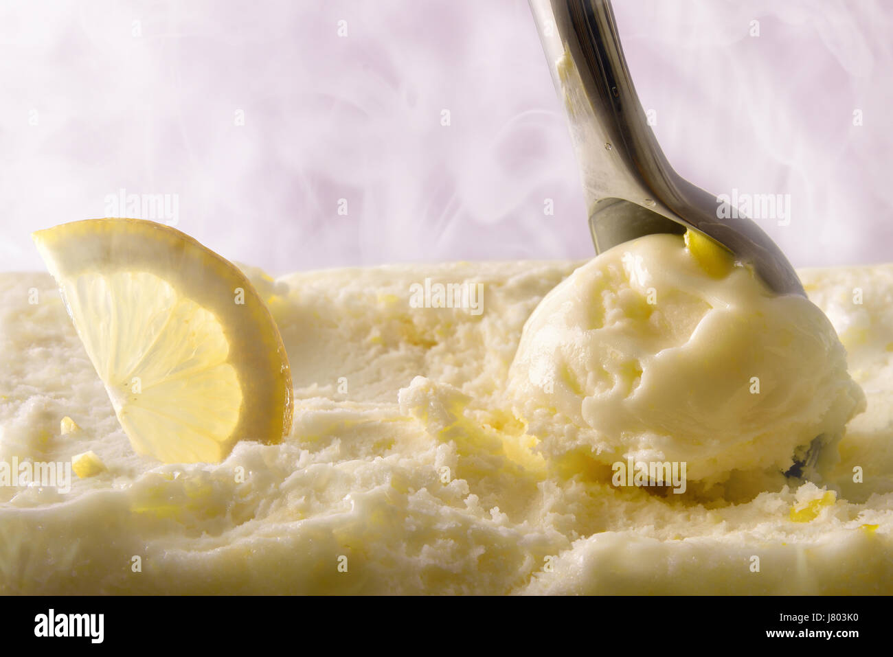 Rendere il gelato al limone sfera vicino. Vista frontale del contenitore per gelato e scoop prelievo di prodotti con frutta. Con vapore freddo in background. Parte anteriore Foto Stock