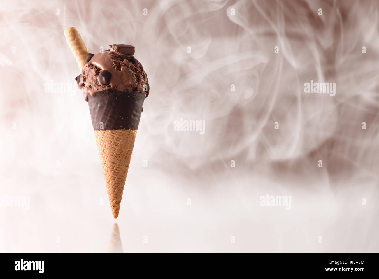 Cono gelato cioccolato aromatizzato. Elevazione sul piano riflettente e guarnita con gocce e le piazze di cioccolato. Con sfondo marrone e freddo stea Foto Stock