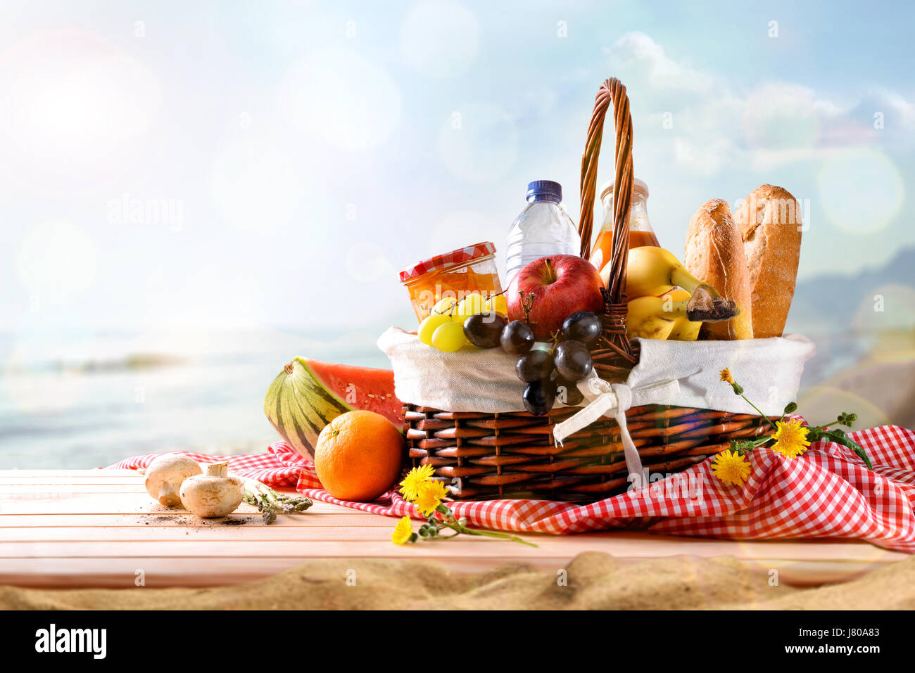Picnic a cesto in vimini con il cibo sulla tavola di legno sulla spiaggia  con cielo blu di sfondo e sun. Il concetto di picnic. Vista frontale.  Composizione orizzontale Foto stock 