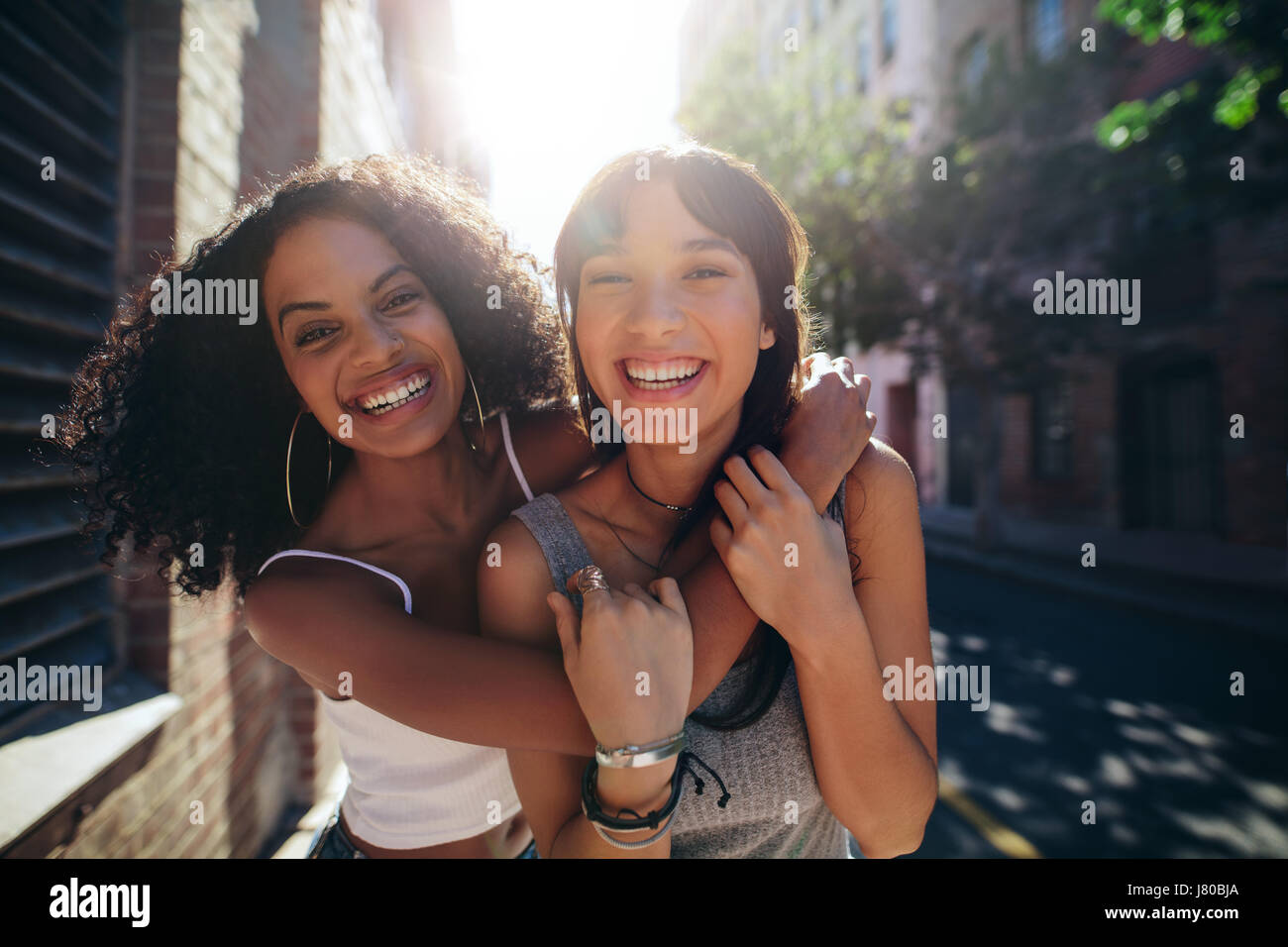 Ritratto di due giovani donne sulla strada di città del divertimento. Amici di sesso femminile sulla strada abbracciando e sorridente all'esterno. Foto Stock
