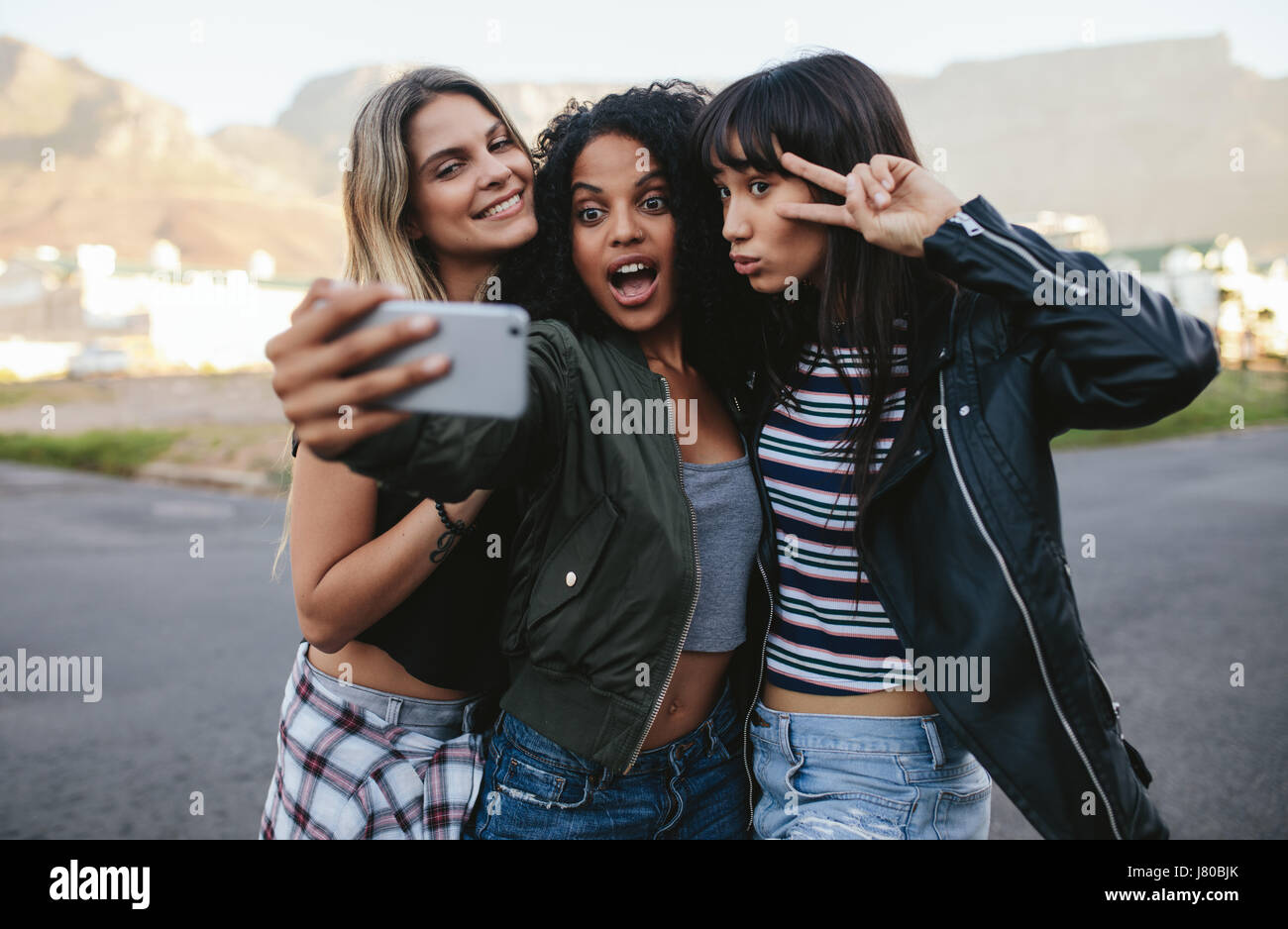 Happy amici di sesso femminile rendendo selfie con smart phone. Multi gruppo etnico di donne appendere fuori città e tenendo autoritratto con il telefono cellulare. Foto Stock