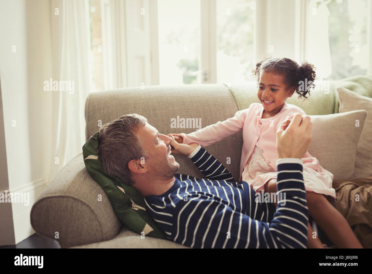 Affettuosa multi-etnico padre e figlia tenendo le mani sul divano Foto Stock