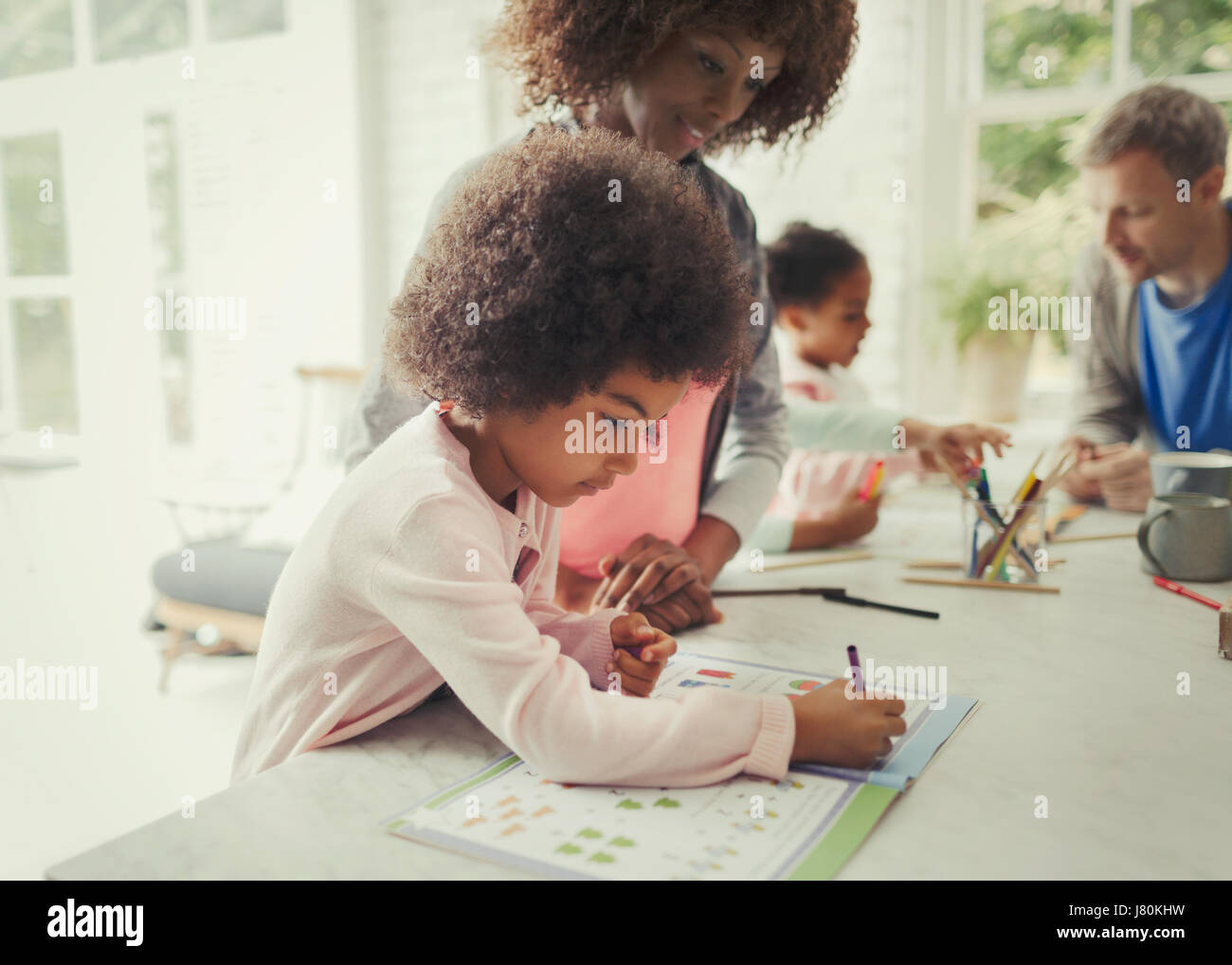 Madre guarda la figlia colorazione in activity book in cucina Foto Stock