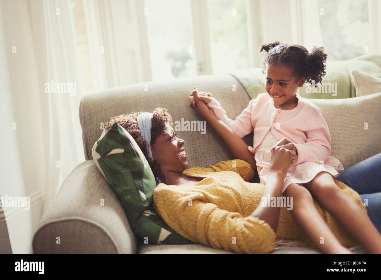 Giocoso madre e figlia tenendo le mani sul divano Foto Stock
