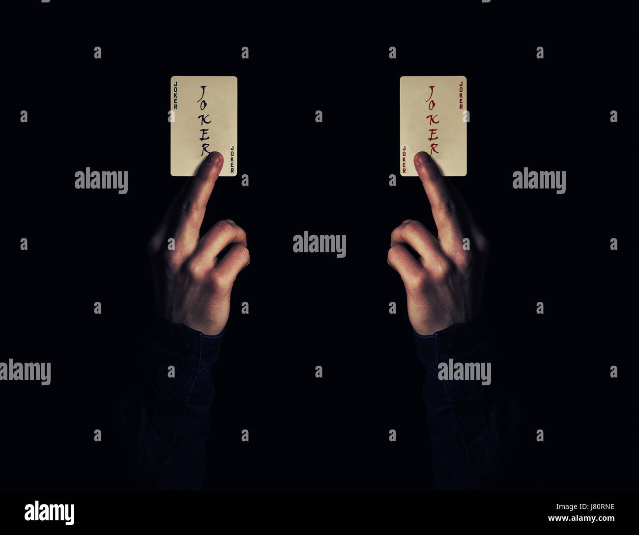 Chiudere fino a due mani di uomo azienda joker carta da gioco. Illusionista mostra un trucco di magia su uno sfondo nero. Gioco del Casino concetto. Foto Stock