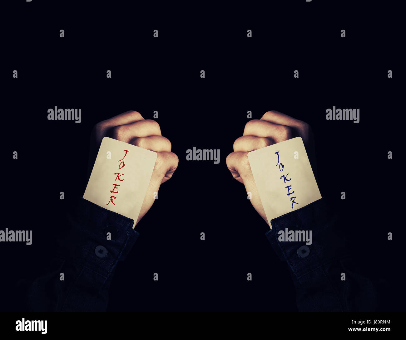 In prossimità dei due pugni holding joker giocando a carte nella manica. Il mago che mostra il suo trucco con carte su uno sfondo nero. Gioco del Casino concetto. Foto Stock