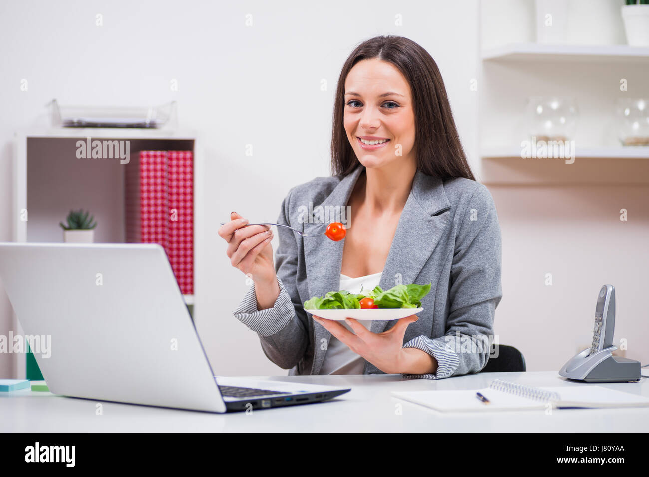 Giovane imprenditrice è mangiare insalata nel suo ufficio. Foto Stock