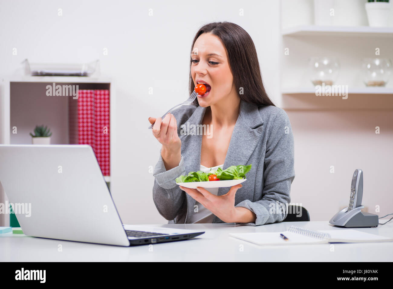 Giovane imprenditrice è mangiare insalata nel suo ufficio. Foto Stock